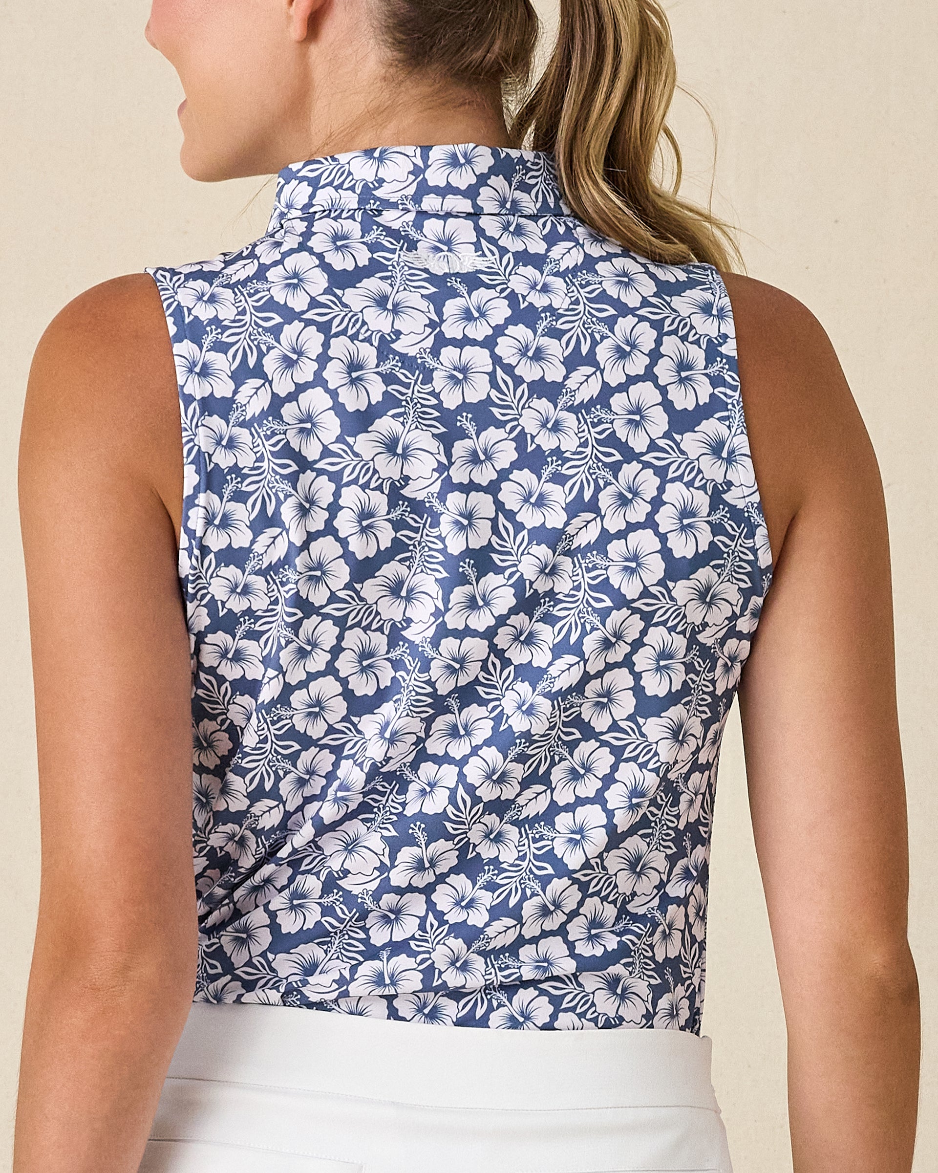 Moloka'i Sleeveless Polo in Moonlight, back view on model featuring a slate blue base with a white hibiscus and tropical leaf print, paired with a white skort