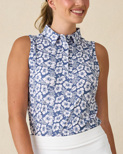Moloka'i Sleeveless Polo in Moonlight, front view on model featuring a slate blue base with a white hibiscus and tropical leaf print, paired with a white skort