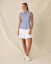Moloka'i Sleeveless Polo in Moonlight, full-length front view on model featuring a slate blue base with a white hibiscus and tropical leaf print, paired with a white pleated skort and white golf shoes
