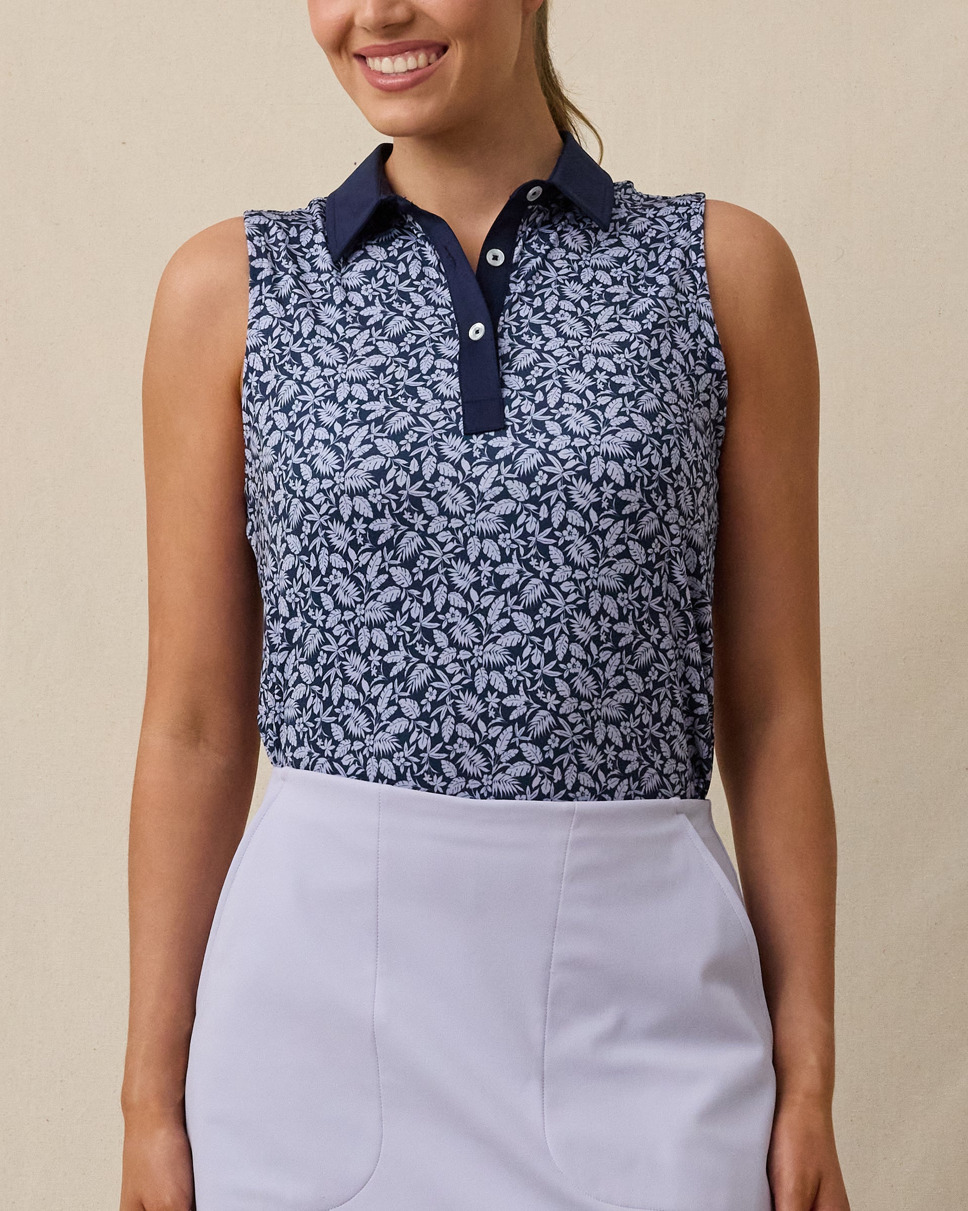 Model wearing the Women's Huli Sleeveless Polo in New Indigo with a tropical leaf and floral print and solid indigo collar