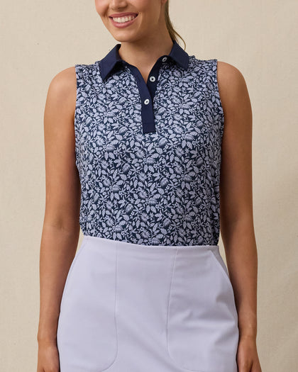 Model wearing the Women's Huli Sleeveless Polo in New Indigo with a tropical leaf and floral print and solid indigo collar