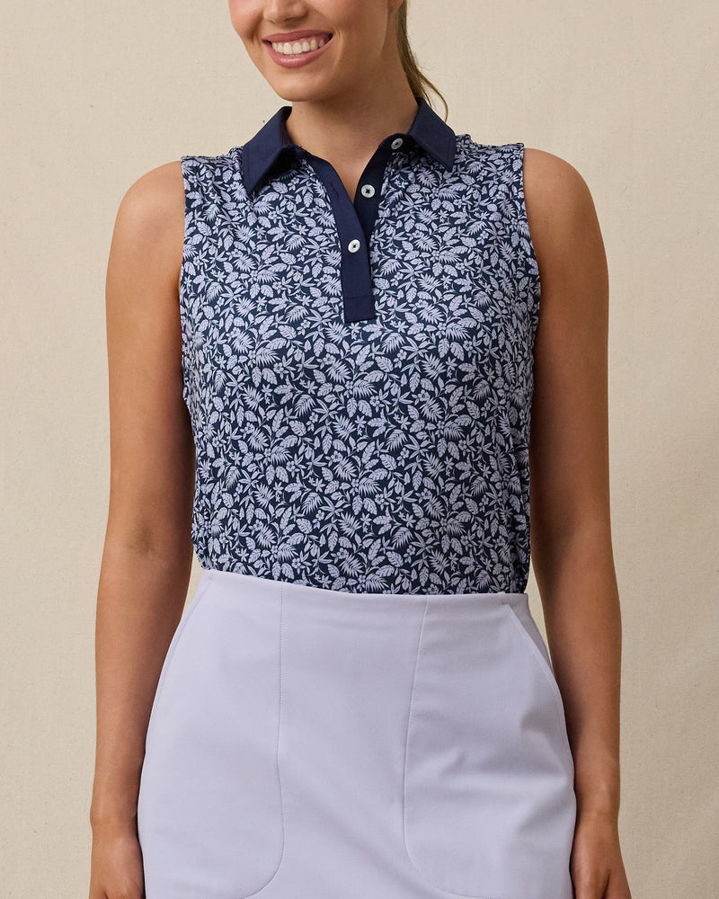 Model wearing the Women's Huli Sleeveless Polo in New Indigo with a tropical leaf and floral print and solid indigo collar