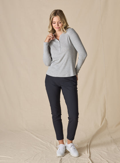 Women’s light grey long sleeve henley top with soft knit fabric, full body front view on model with button placket neckline, and ribbed cuff paired with black pants and white shoes