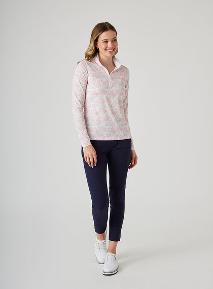 Alabama Quarter Zip in Flamingo, full-length front model view featuring a white long-sleeve pullover with an allover pink floral and grey leaf print, quarter zip, and white mock neck collar, paired with navy cropped pants and white shoes