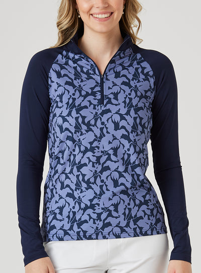 Mabel Quarter Zip in New Indigo, front model view featuring a long-sleeve pullover with an allover navy and blue abstract floral print body, solid navy raglan sleeves, quarter zip, and navy mock neck collar, paired with white pants