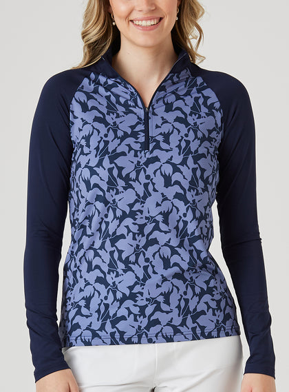 Mabel Quarter Zip in New Indigo, front model view featuring a long-sleeve pullover with an allover navy and blue abstract floral print body, solid navy raglan sleeves, quarter zip, and navy mock neck collar, paired with white pants