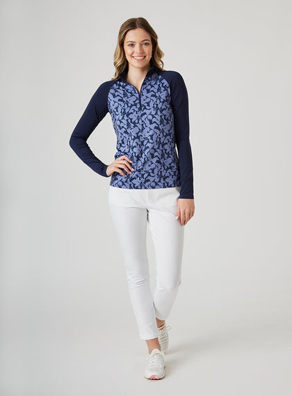 Mabel Quarter Zip in New Indigo, full-length front model view featuring a long-sleeve pullover with an allover navy and blue abstract floral print body, solid navy raglan sleeves, quarter zip, and navy mock neck collar, paired with white cropped pants and white shoes