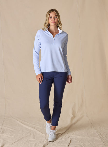 Women's Ellen Quarter Zip in Powder, full-length front view on model featuring a soft powder blue textured performance fabric with a quarter-zip stand collar, raglan sleeves, and white zipper detail, paired with navy pants and white shoes