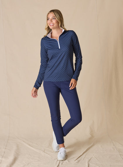 Dottie Quarter Zip in Cedar, full-length front model view featuring a navy long-sleeve pullover with an allover pink polka dot print, quarter zip, and white mock neck collar with white interior lining, paired with navy cropped pants and white shoes