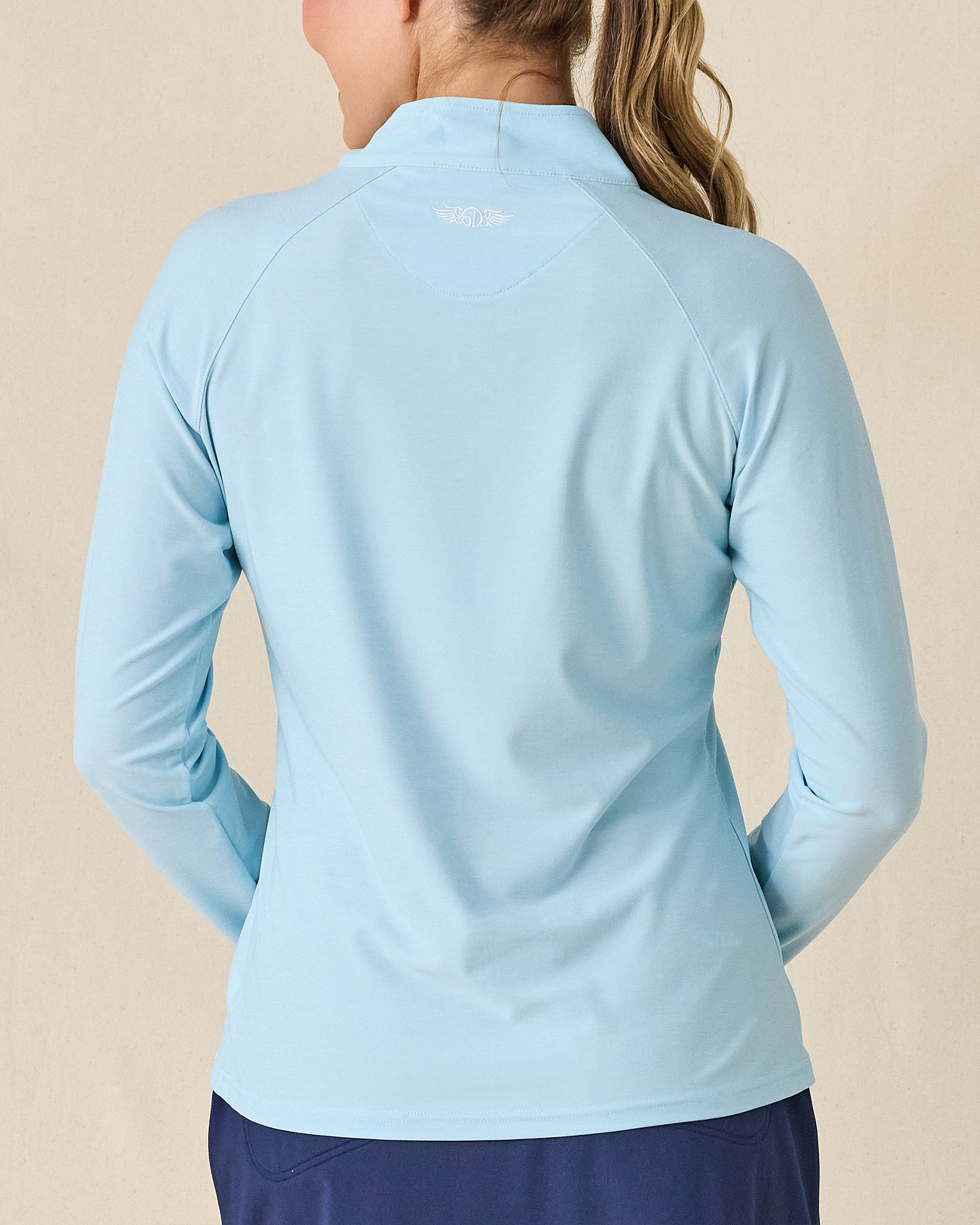Clara Quarter Zip in Gemstone, back view featuring a solid light blue long sleeve pullover with Straight Down embroidered logo at the upper back, paired with navy pants