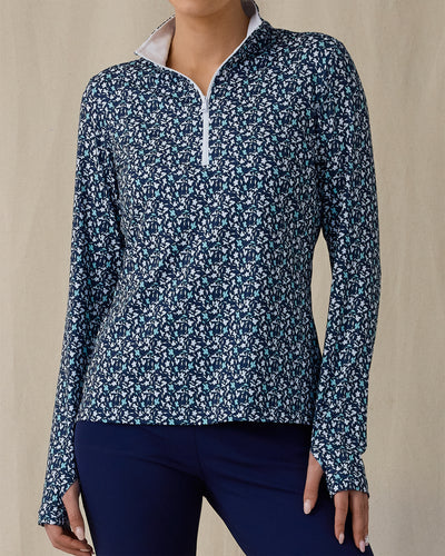 Women's Flores Quarter Zip in New Indigo, front on-model view from the waist up featuring a navy long sleeve quarter zip pullover with an allover small floral print in white and mint green tones, mock neck collar, and white zipper, paired with navy pants