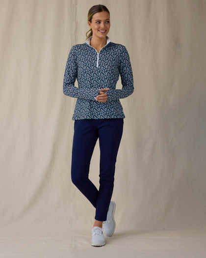 Women's Flores Quarter Zip in New Indigo, full-length front on-model view featuring a navy long sleeve quarter zip pullover with an allover small floral print in white and mint green tones, mock neck collar, and white zipper, paired with navy pants and white shoes