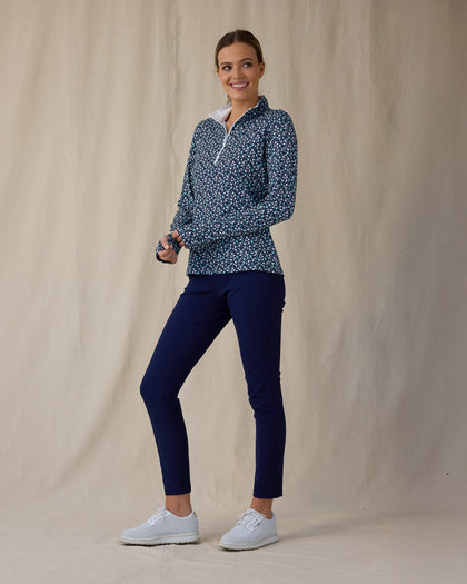 Women's Flores Quarter Zip in New Indigo, full-length front on-model view with a relaxed stance featuring a navy long sleeve quarter zip pullover with an allover small floral print in white and mint green tones, mock neck collar, and white zipper, paired with navy pants and white shoes