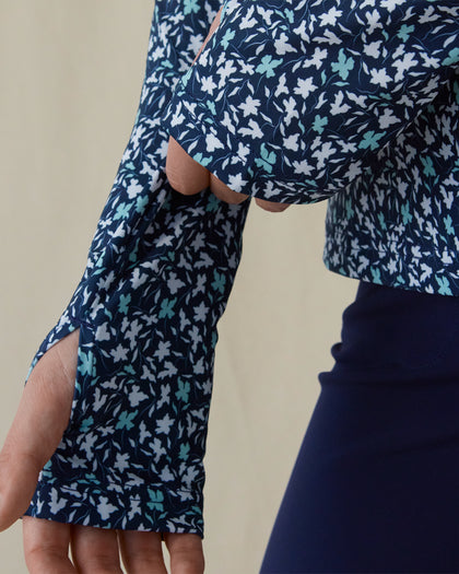 Women's Flores Quarter Zip in New Indigo, close-up on-model view highlighting the thumb hole cuff detail on the long sleeve featuring an allover small floral print in white and mint green tones on a navy base