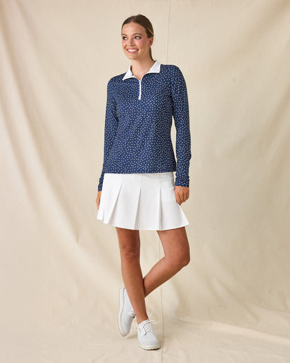 Cherry Bloom Quarter Zip in New Indigo, full-length side-angle view on model featuring a navy base with a scattered white and pink floral print, paired with a white pleated skort and white golf shoes