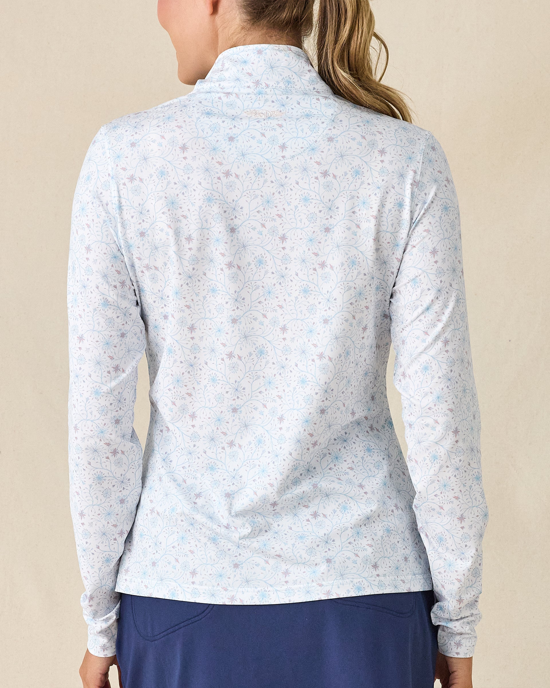 Mariette Quarter Zip in Gemstone, back view featuring a white base with light blue and mauve floral vine allover print pattern with Straight Down embroidered logo at the upper back, paired with navy pants