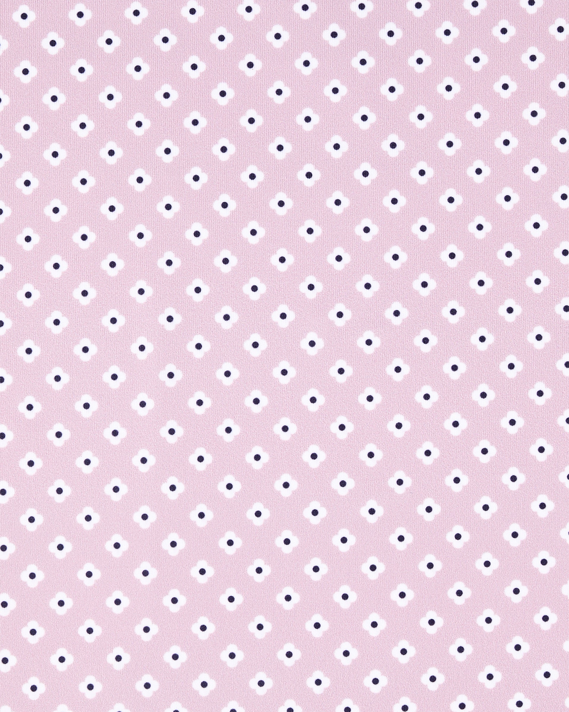 A close-up of a light pink fabric or material with a repeating pattern of small white and dark navy dots.