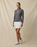 Full-length front view of a woman wearing the Skyler Quarter Zip in Nightshade zipped to the top, paired with a white pleated skort and white golf shoes.