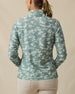 Back view of a woman wearing a lighter and darker green camouflage quarter-zip top, showing the long sleeves, stand collar, and light peach logo below the back neckline.