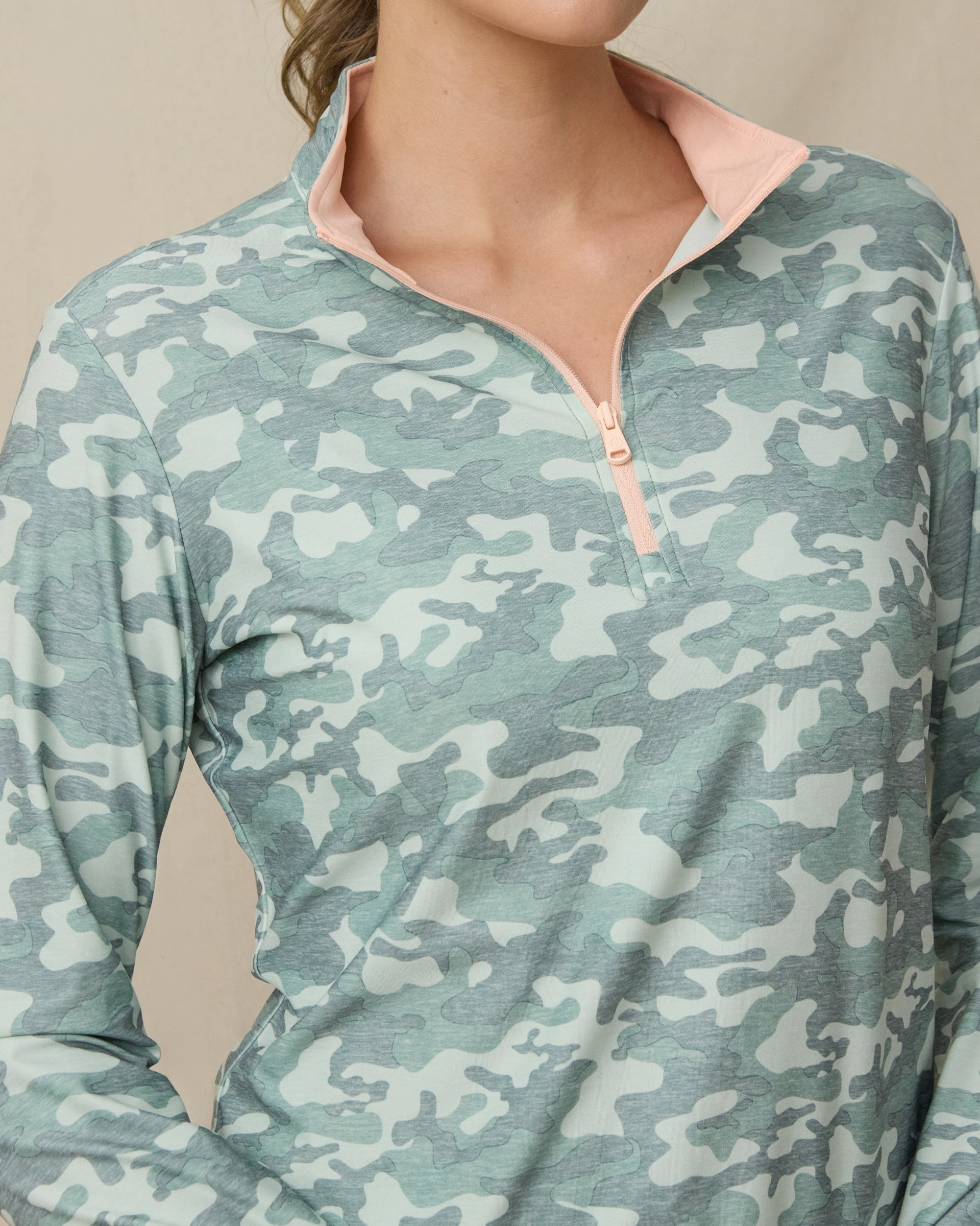 Close-up of the green camouflage quarter-zip top showing the light peach zipper and contrasting light peach interior collar.