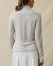 Back view of a woman wearing a light blue pastel floral quarter-zip top, showing the long sleeves, stand collar, and subtle logo below the back neckline.