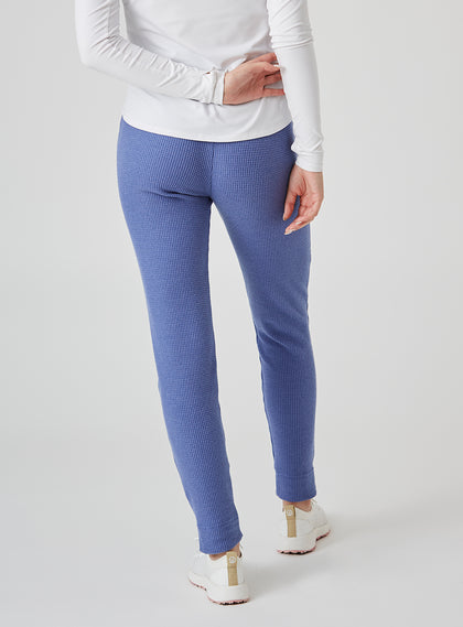 Women's Mavis Jogger in Blueberry, back model view featuring a medium blue waffle-knit jogger with elasticated waistband, clean back panel, and tapered leg with cuffed hem paired with a white long sleeve top and white athletic shoes