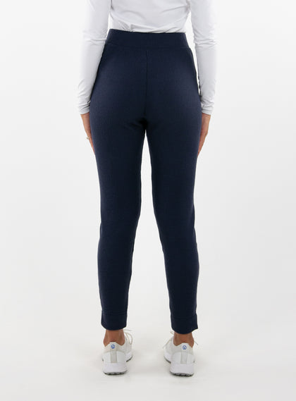 Women's Mavis Jogger in Ink, back model view featuring a navy waffle-knit jogger with elasticated waistband, clean back panel, and tapered leg with cuffed hem paired with a white long sleeve top and white athletic shoes