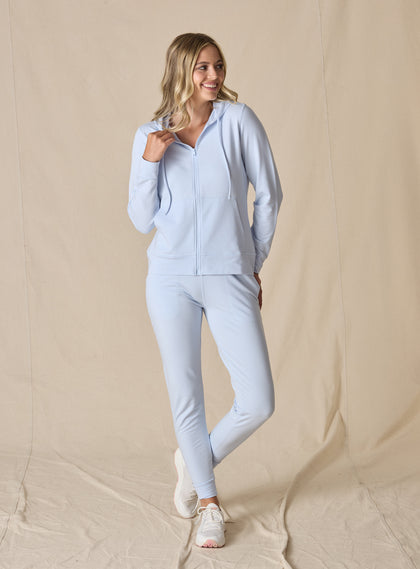 Women's Topia Jogger in Powder, full length model view featuring a soft blue smooth-knit jogger paired with a matching Mesa Hooded Jacket and white athletic shoes