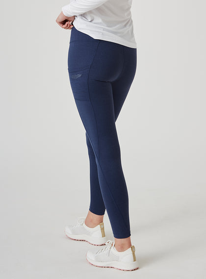 Sedona Legging in New Indigo, on model side view showing the solid navy high-waisted legging with Straight Down logo on the side pocket, styled with a white long sleeve top and white shoes