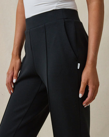 Close-up of a model wearing black high-waisted wide-leg trousers with a white top, against a neutral beige background.