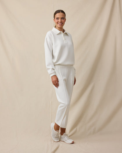 Woman wearing the Chelsea Pant in Coconut with a coordinating off-white long-sleeve top and white sneakers.