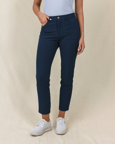 Stride Pant in New Indigo, front close-up view on model in solid navy with a gold snap closure and front pockets, paired with white golf shoes