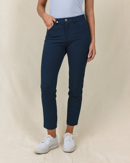Stride Pant in New Indigo, front close-up view on model in solid navy with a gold snap closure and front pockets, paired with white golf shoes