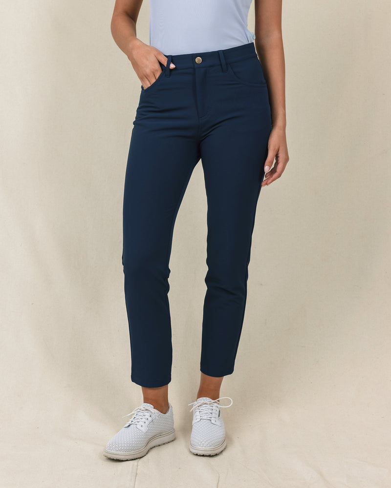 Stride Pant in New Indigo, front close-up view on model in solid navy with a gold snap closure and front pockets, paired with white golf shoes