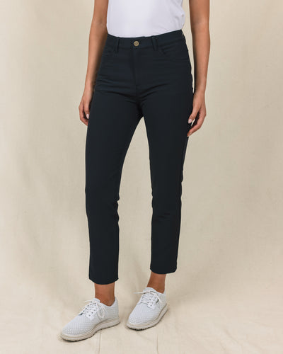 Women's Stride Pant in Black, front view on model featuring black ankle-length pants with high rise waist and gold button closure, paired with a white top and white golf shoes