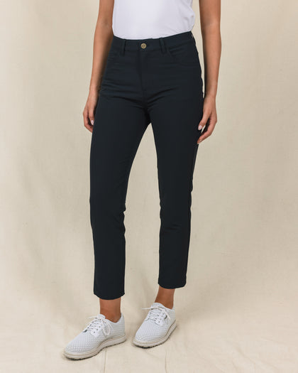 Women's Stride Pant in Black, front view on model featuring black ankle-length pants with high rise waist and gold button closure, paired with a white top and white golf shoes