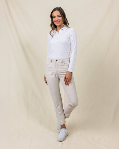 Women's Stride Pant in Stone, full length front view on model featuring a stone colored ankle pant with front patch pockets, paired with a white long sleeve polo and white golf shoes
