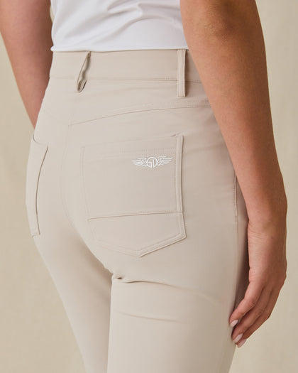 Close-up of a model wearing beige pants, showing the back pocket with a white embroidered winged logo and a white top.