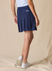 Women's Martina Skort in New Indigo, back view on model featuring a navy pleated skort with a wide waistband, back pockets, and embroidered Straight Down logo paired with a light blue sleeveless top and white golf shoes