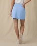 Evie Skort in Carolina, back view on model showing a light blue skort with back patch pocket and Straight Down logo, paired with a white polo and white golf shoes