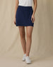 Evie Skort in New Indigo, front view on model showing a navy skort with front patch pockets, paired with a white polo and white golf shoes