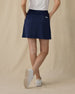 Evie Skort in New Indigo, back view on model showing a navy skort with back patch pocket and Straight Down logo, paired with a white polo and white golf shoes