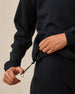 Close-up of A woman modeling a black sweatshirt and matching black bottoms, pulling the drawstring of the waistband with one hand while the other hand rests near the side.