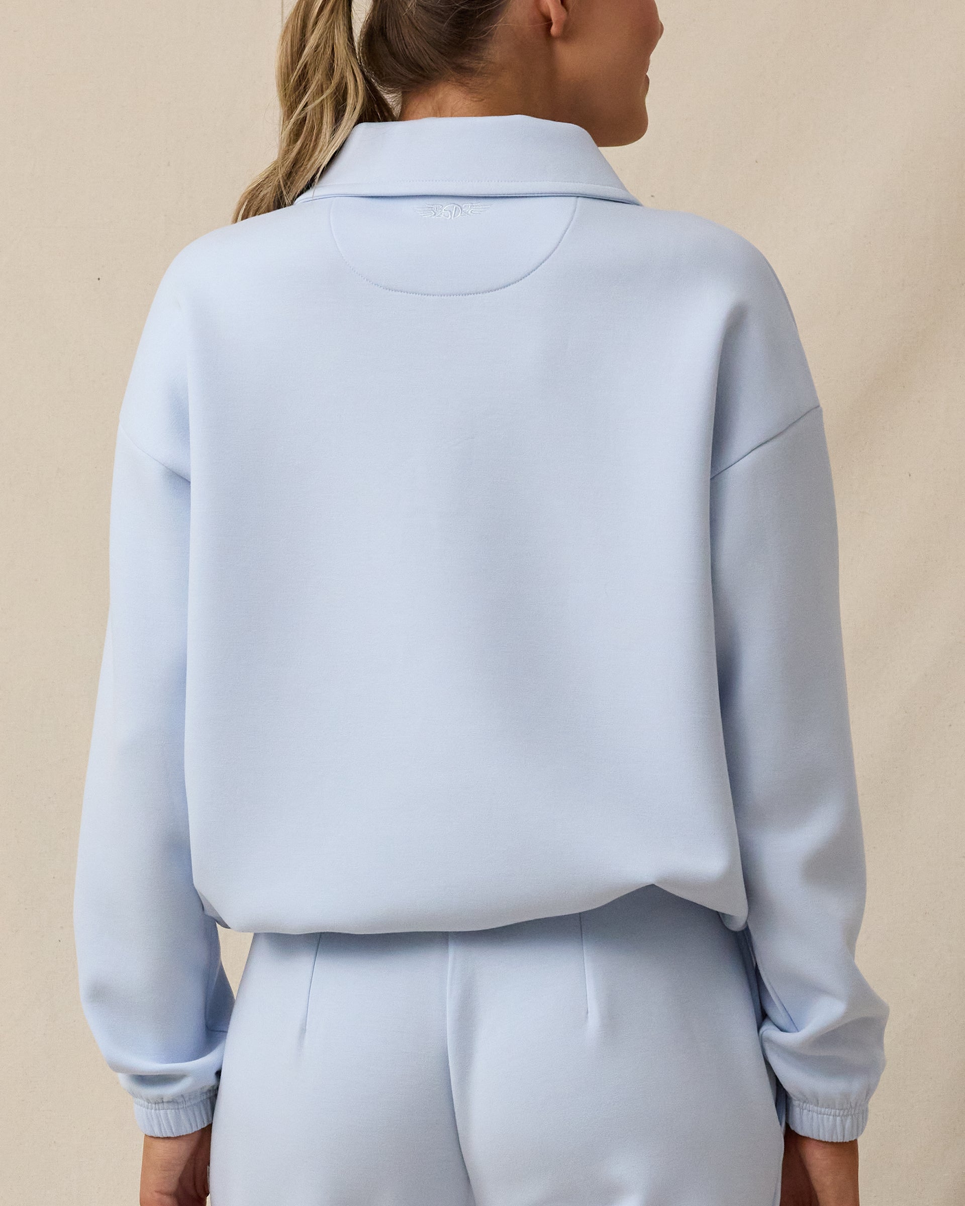 A woman modeling from the back wearing a light blue cropped long-sleeve top and matching light blue bottoms.