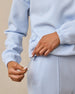 A close-up of a person wearing a light blue sweatshirt and matching pants, pulling the drawstring of the sweatshirt.