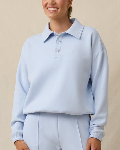 A woman modeling a light blue long-sleeve polo sweatshirt and matching light blue pants.
