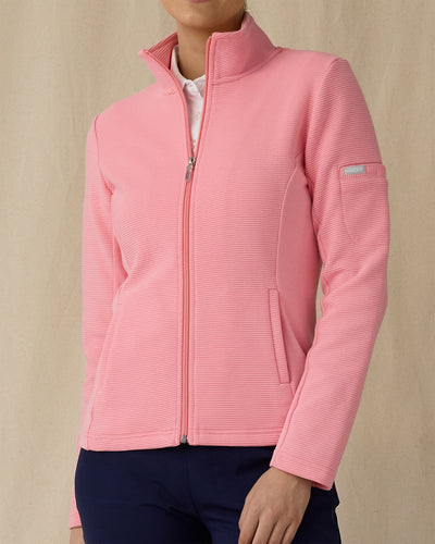Women's Swing Jacket in Geranium, front view on model featuring a pink full zip jacket with a ribbed texture and stand collar, paired with a white polo and navy pants
