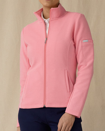 Women's Swing Jacket in Geranium, front view on model featuring a pink full zip jacket with a ribbed texture and stand collar, paired with a white polo and navy pants