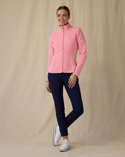Women's Swing Jacket in Geranium, full length front angle view on model featuring a pink full zip jacket with a ribbed texture and stand collar, paired with navy pants and white golf shoes