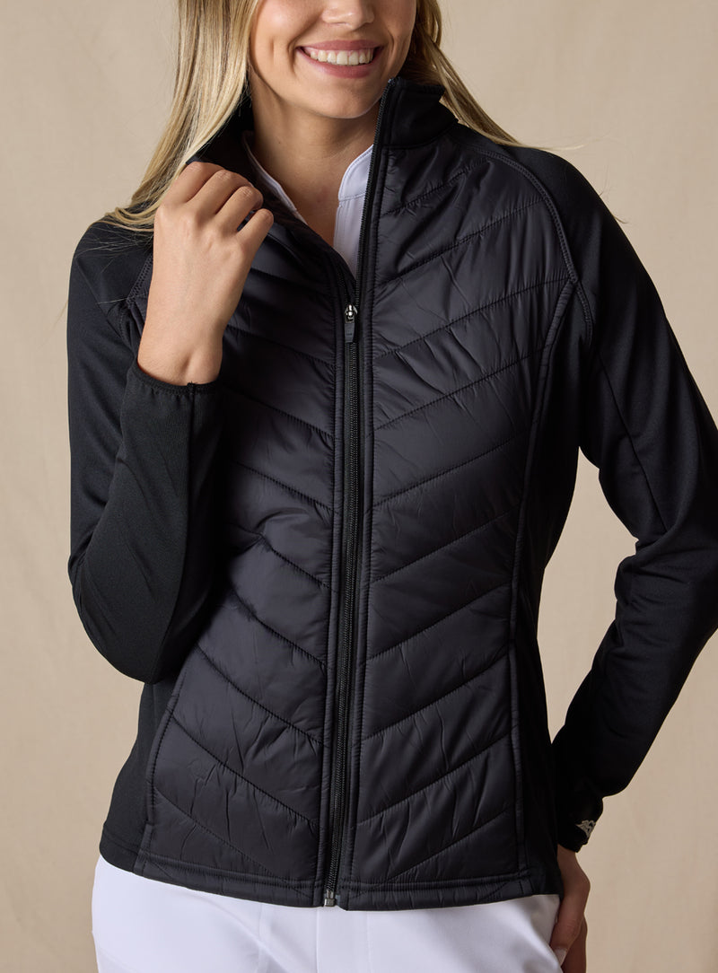 Nova Jacket in Black, front view on model featuring a black hybrid full-zip jacket with diagonal quilted body, stretch knit sleeves, and mock neck collar styled with white pants